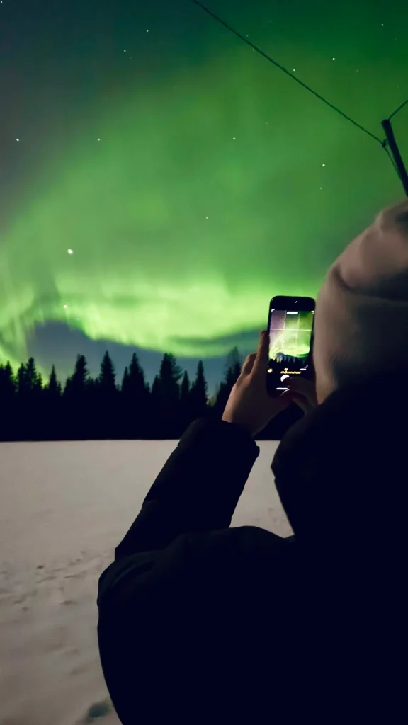 Person photographing the northern lights on a smartphone during a Lapland aurora tour